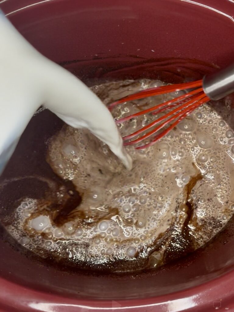 milk being poured into cocoa mixture in a slow cooker